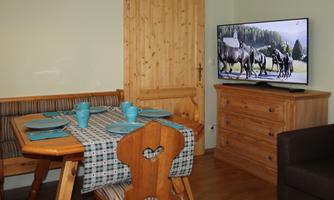 A cozy dining area with a wooden table, chairs, and blue dishware. In the background, there is a TV showing a nature film.