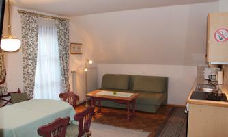 A cozy living space with a green sofa and a small dining table. The decor is bright and friendly, with a small kitchen area in the corner.