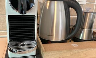 A modern Nespresso machine stands next to a kettle on a countertop. Tiles are visible in the background.