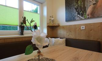 A cozy room with a wooden table and a seating area. On the table sits a decorative flower in a vase.