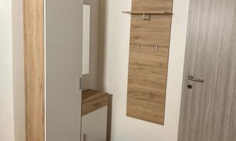 A modern hallway with a white cabinet and a wooden shelf. The walls are light and the floor is made of wood.