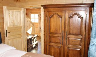 A cozy wooden interior with a large, classic wardrobe. In the background, a staircase and a window are visible.