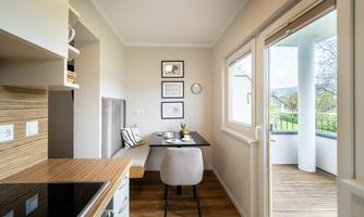 A modern dining room with a small table and a cozy bench. Large windows provide a view outside and plenty of daylight.