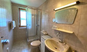 A modern bathroom with a shower, sink, and toilet. The walls are lined with bright tiles and there is a window for natural light.