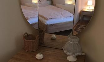 A cozy room with a large mirror and a wooden cabinet. In the background, a bed and soft lighting are visible.