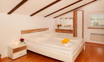 A bright bedroom with a large double bed and a modern piece of furniture. The walls are white and the wooden beams give the room a cozy atmosphere.