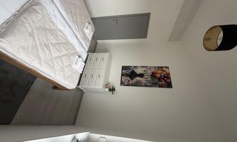A modern bedroom with a large bed and a compact dresser. A colorful painting with balloons hangs on the wall.