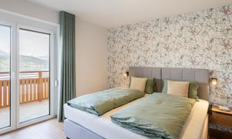 A modern room with two beds and cozy bed linen. Large windows offer a view of the landscape and plenty of daylight.