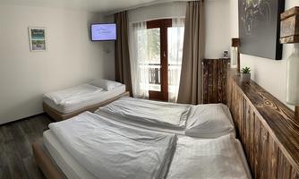 A cozy room with two beds and wooden details. There is a TV, a balcony, and plenty of daylight.