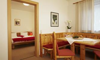 A cozy apartment with a dining area and a bedroom in the background. The décor is made of wood and is bright and inviting.