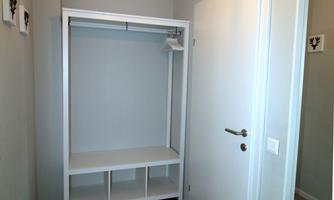 A bright hallway with an open wardrobe and a large mirror. The walls are painted in soft gray tones, and a lamp hangs from the ceiling.
