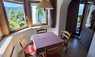 A cozy dining area with a table and chairs. Large windows provide a lovely view of nature outside.