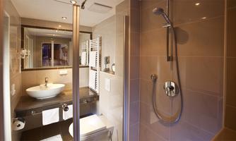 A modern bathroom with a shower and a sink. The walls are light and the decor is elegant and functional.