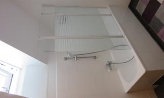 A modern bathroom with a bathtub and a shower partition. The window provides plenty of daylight.
