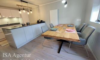 A modern dining room with a large wooden table and comfortable chairs. The kitchen is in an open area and well-equipped.