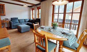 A cozy living area with a blue sofa and a dining table. Large windows provide plenty of daylight and a view outside.