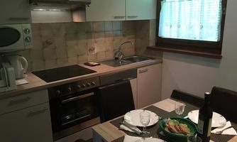 A modern kitchen with an electric stove, microwave, and a sink. The table is set for four people and decorated with dishes and a bottle of wine.