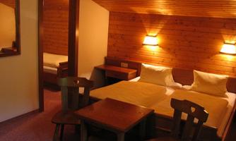 A cozy room with two beds and wood paneling. There is a small table with chairs and a mirrored wall.