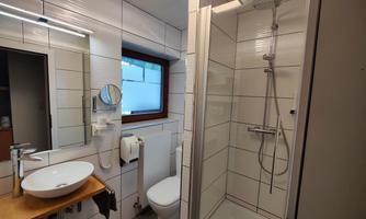 A modern bathroom with a shower, sink, and toilet. Bright tiles and a window create an inviting atmosphere.