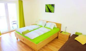 A bright bedroom with a double bed and a cozy sofa bed. The walls are in neutral colors, and there are green accents with curtains and bedding.