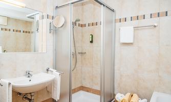 A modern bathroom with a shower and a sink. There are towels and toiletries neatly arranged on the shelf.