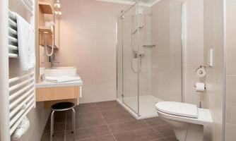 A modern bathroom with a glass shower and a sink. The walls are in light tones, and there is a towel radiator.