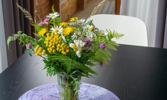 A beautiful bouquet of flowers in a glass stands on a table. In the background, you can see a balcony with windows and wooden elements.
