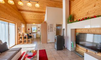 A bright, modern living room with wood paneling and large windows. There is a comfortable sofa, a television, and a cozy atmosphere.