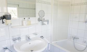 A modern bathroom with white tiles and a shower. There is a sink, a bathtub, and toiletries on the shelf.