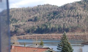 A tranquil lake, surrounded by wooded hills. The landscape is calm and inviting.