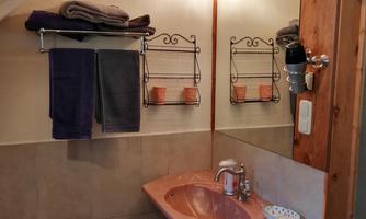 Bathroom with rose quartz washbasin under a sloped ceiling, mirror with lighting, towel shelf with folded towels and wall rack.
