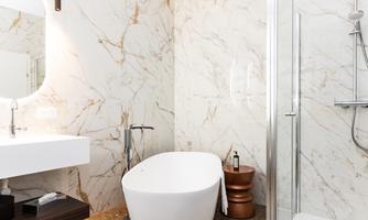 A modern bathroom with marbled walls. It includes a freestanding bathtub and a shower.