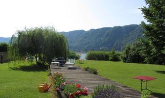 A beautiful garden with well-kept grass and colorful flowers. In the background, mountains and a lake are visible.