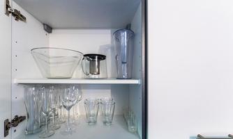 An open kitchen cabinet with various jars and a bowl. The storage is neat and structured.