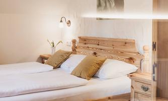 A cozy bedroom with two beds and wooden details. The decoration is simple and inviting, with neutral colors and soft cushions.