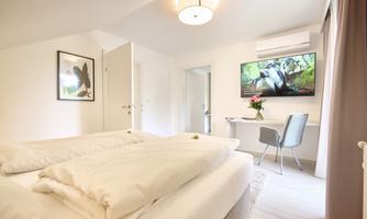 A modern room with two beds and a television on the wall. The room is brightly and pleasantly furnished.