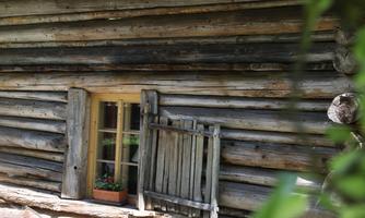A rustic wooden house with shutters and a blooming flower box. The walls are made of natural wooden logs.