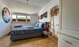 A cozy bedroom with a double bed and modern wall art. The room has large windows that let in a lot of light.