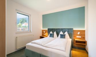 A modern bedroom with a double bed and two pillows. The walls are in soft colors and there is a window with a view outside.