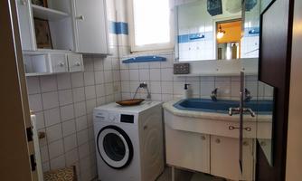 A small bathroom with a washing machine and a sink. There are some shelves and a large mirror.