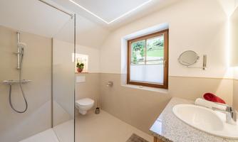 A modern bathroom with a walk-in shower and a window cutout for natural light. The walls are bright, and the furnishings are simple and functional.