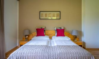 A cozy bedroom with two single beds and red pillows. The walls are light, and the furniture is made of wood.