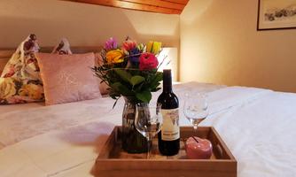 A cozy bedroom with a bed and colorful flowers in a vase. On a tray, there is a bottle of wine, glasses, and a candle.
