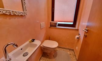 A small bathroom with a modern toilet and a sink. The walls are painted in a warm peach tone and a window provides daylight.
