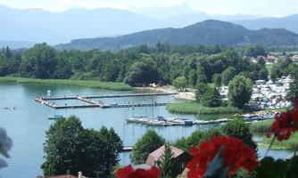 A beautiful lake with boats and a pier. In the background, green forests and mountains can be seen.