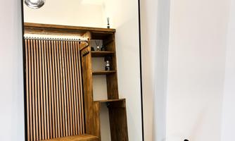 A modern hallway with a large mirror and a wooden shelf. The decor is simple and elegant with warm wooden tones.