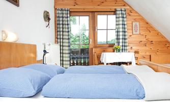 A cozy bedroom with two single beds and blue cushions. In the background, there is a table and a beautiful view through the window.