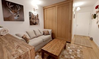 A cozy living room with a beige sofa and a wooden table. Animal portraits hang on the wall and the wooden cabinet provides additional storage space.