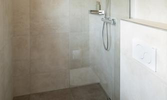 A modern bathroom with an open shower and a toilet. The room is bright and clear, with neutral tiles.