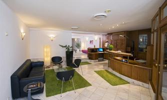 A modern designed reception area with a sofa landscape and a reception desk. Green carpets create a cozy atmosphere.